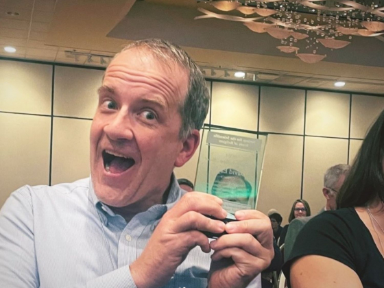 Close up of David Eagle with wide smile holding glass award next to his face 
