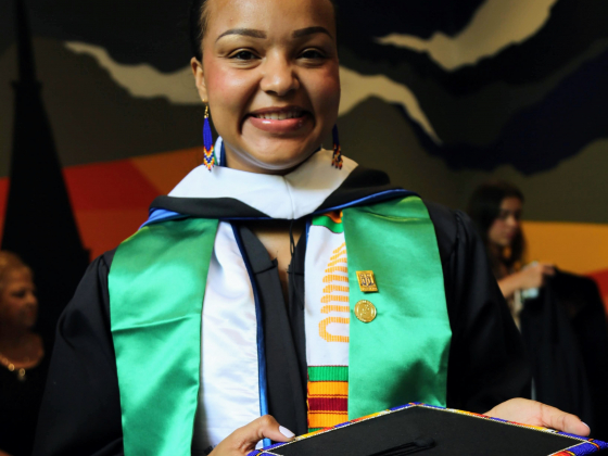 Portrait photo of sociology student Gianni Lacey-Howard wearing graduation gown and multiple stoles and holding decorated graduation cap.