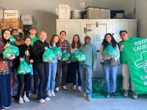 Group photo of Bass Connections students holding bags of food, supplies and a sign reading Root Causes