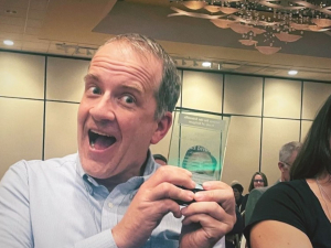 Close up of David Eagle with wide smile holding glass award next to his face 